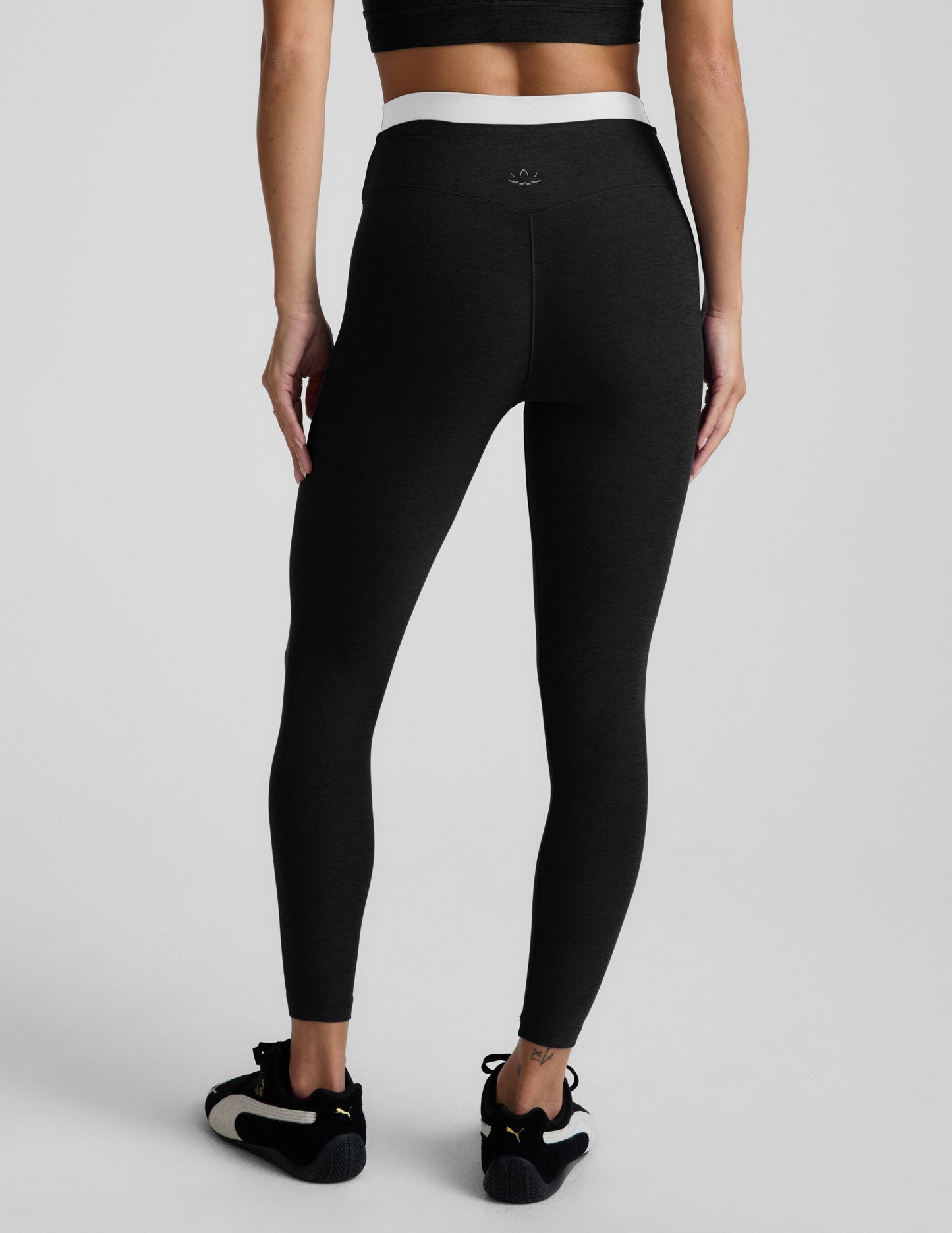 Person wearing black leggings and black athletic shoes on a light gray background.
