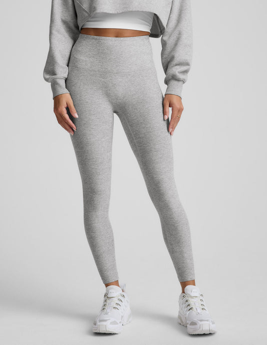 Woman wearing a gray sweatshirt and leggings set on a plain background.