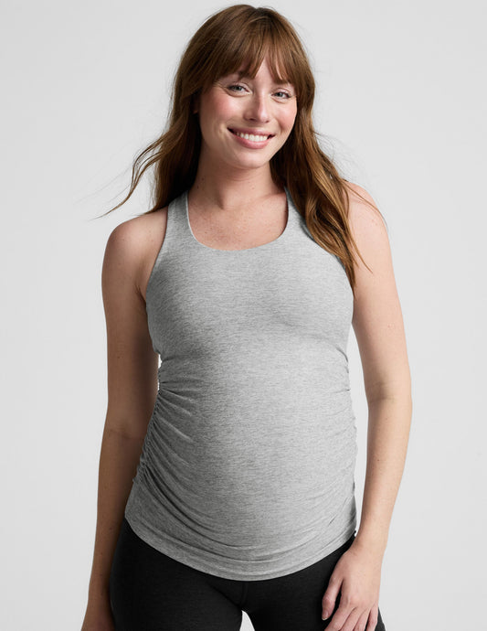 Woman wearing a gray maternity tank top and black shorts on a white background.