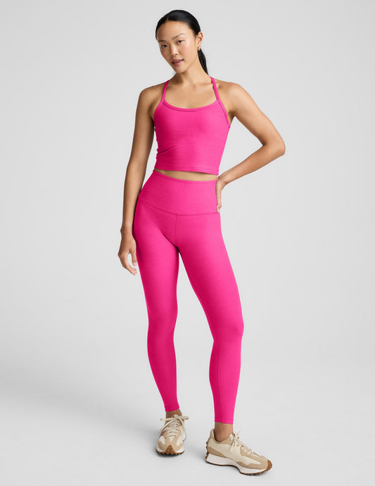 Woman wearing a bright pink cropped tank and leggings on a light gray background.