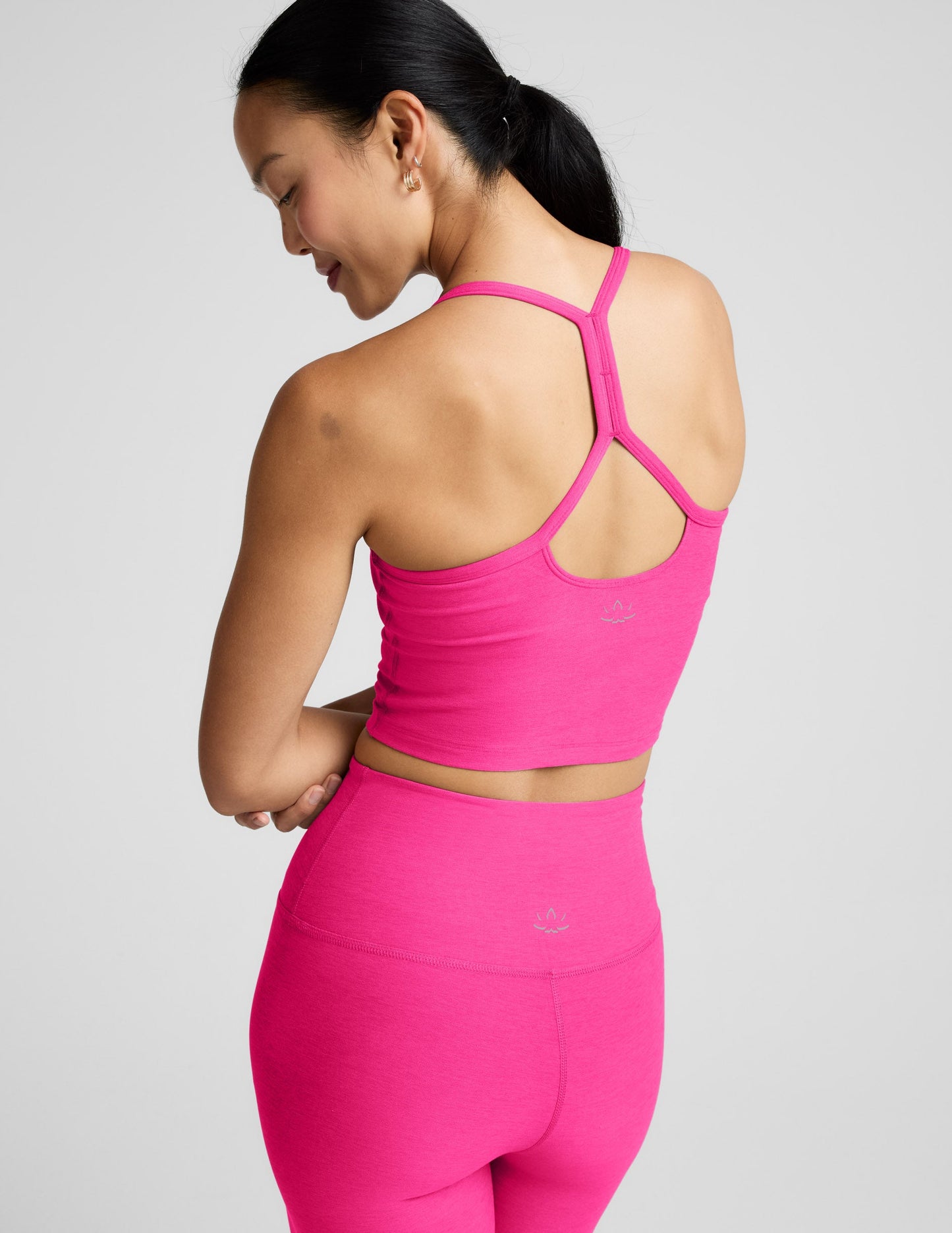 Woman wearing a bright pink cropped tank and leggings on a light gray background.