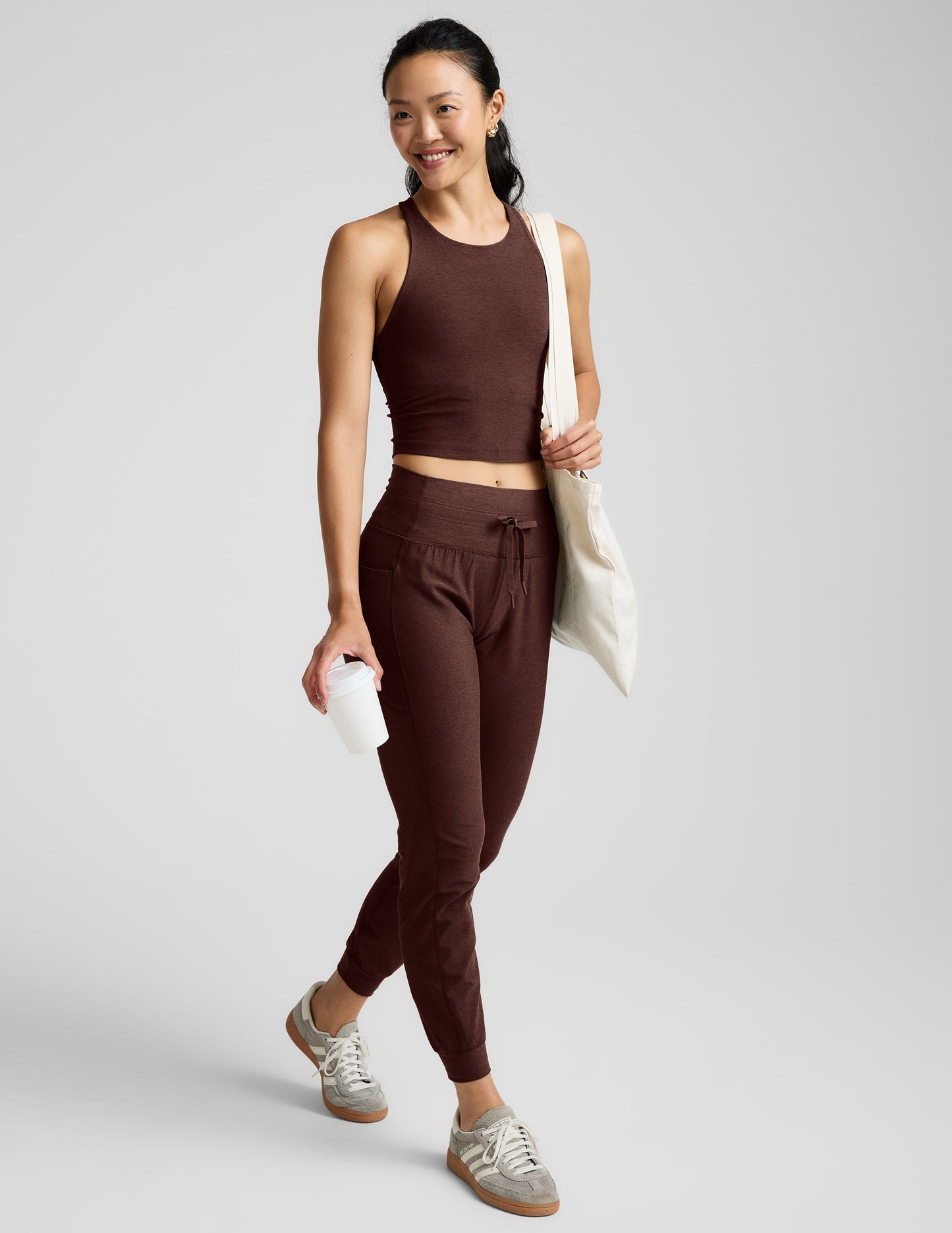 Woman wearing a brown high-neck racerback cropped tank and joggers against a plain background.