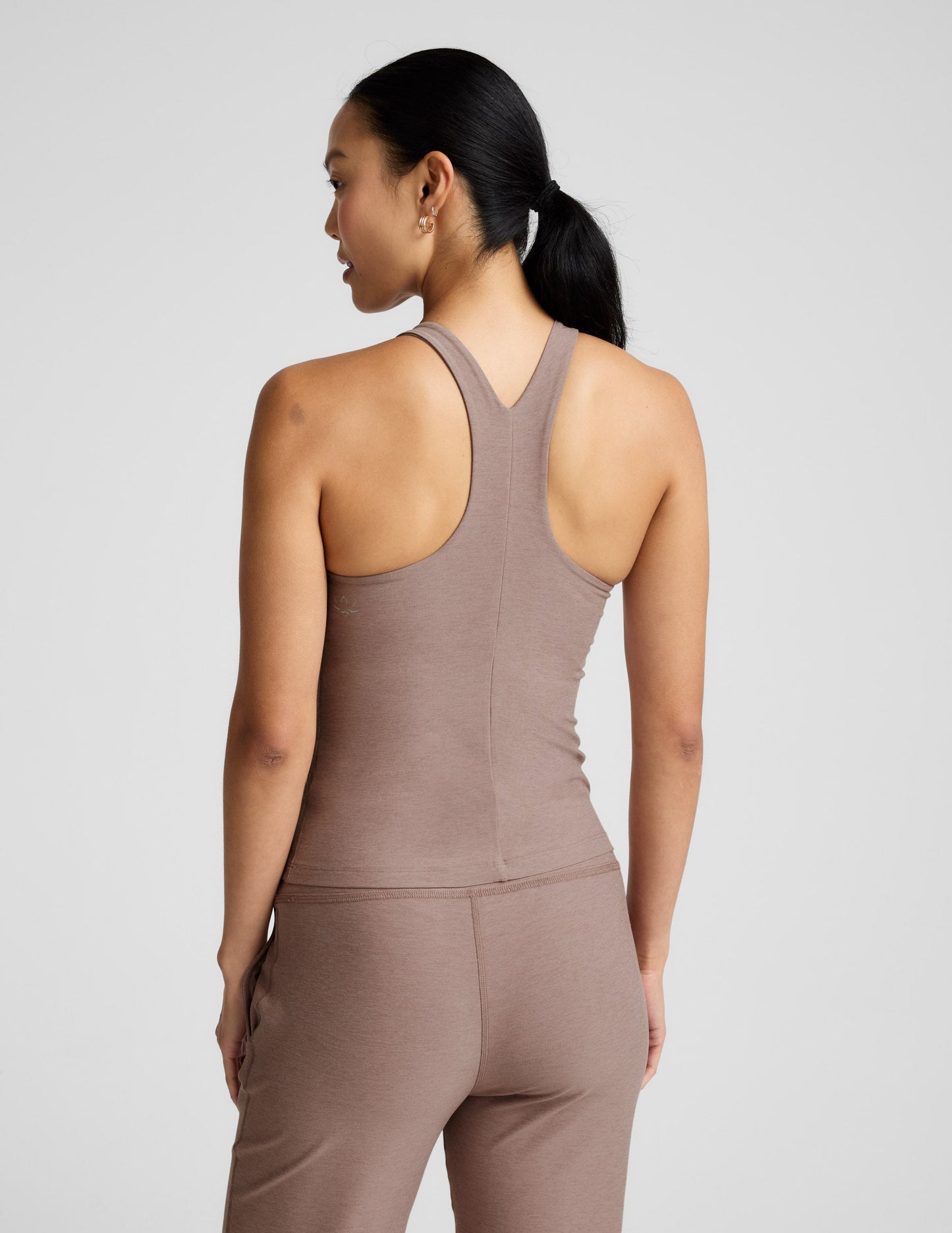 Woman wearing a brown high-neck tank top and pants against a plain background.