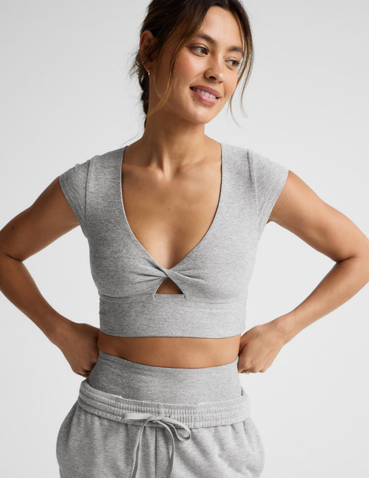 Woman wearing a gray cropped twist tee and sweatpants on a light gray background.