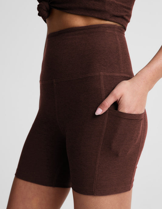 Woman wearing Brown Spacedye™ Keep Pace 5" Pocket Short in a side profile with hand in pocket and matching tied top.