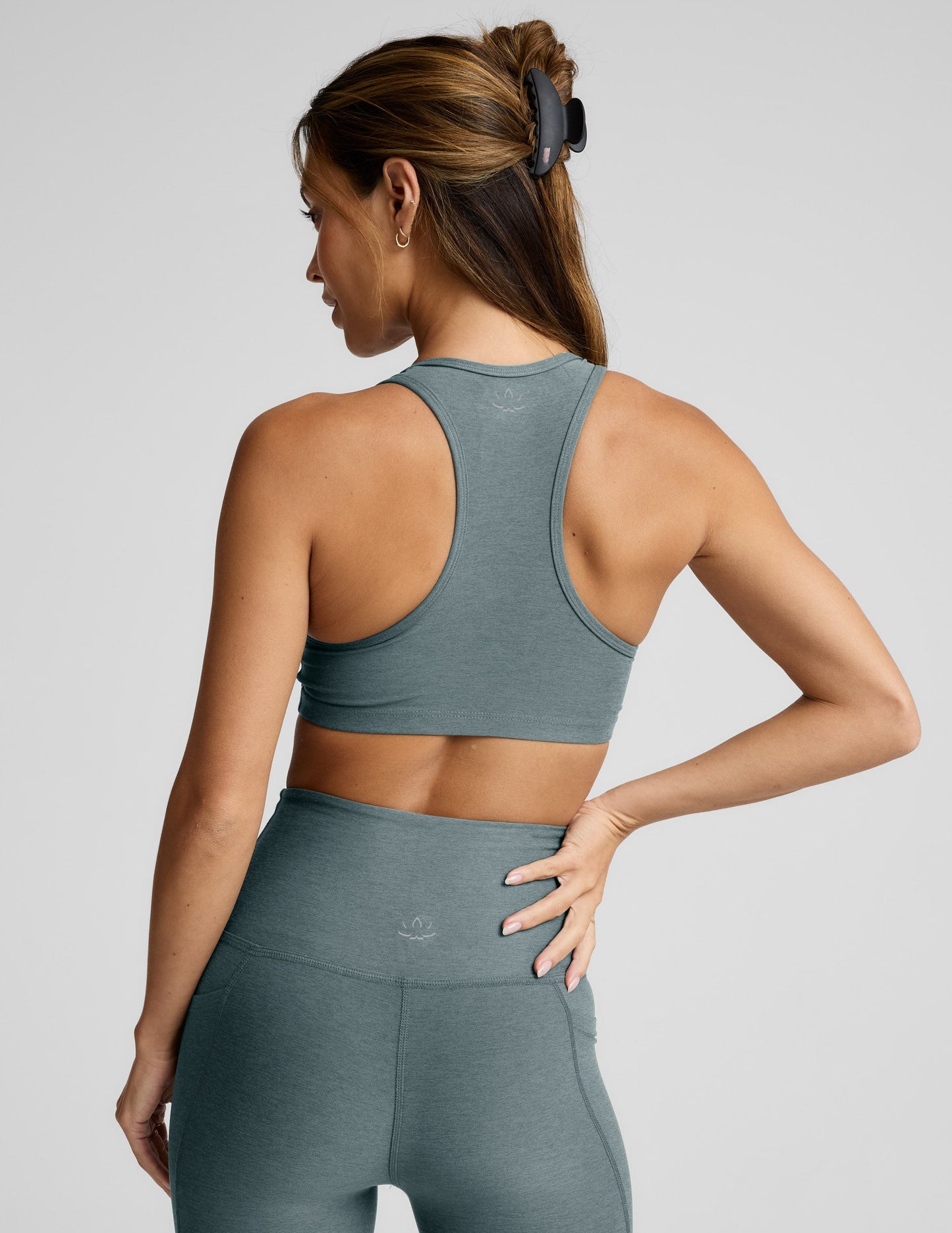 Woman wearing a gray sports bra and leggings on a light gray background.