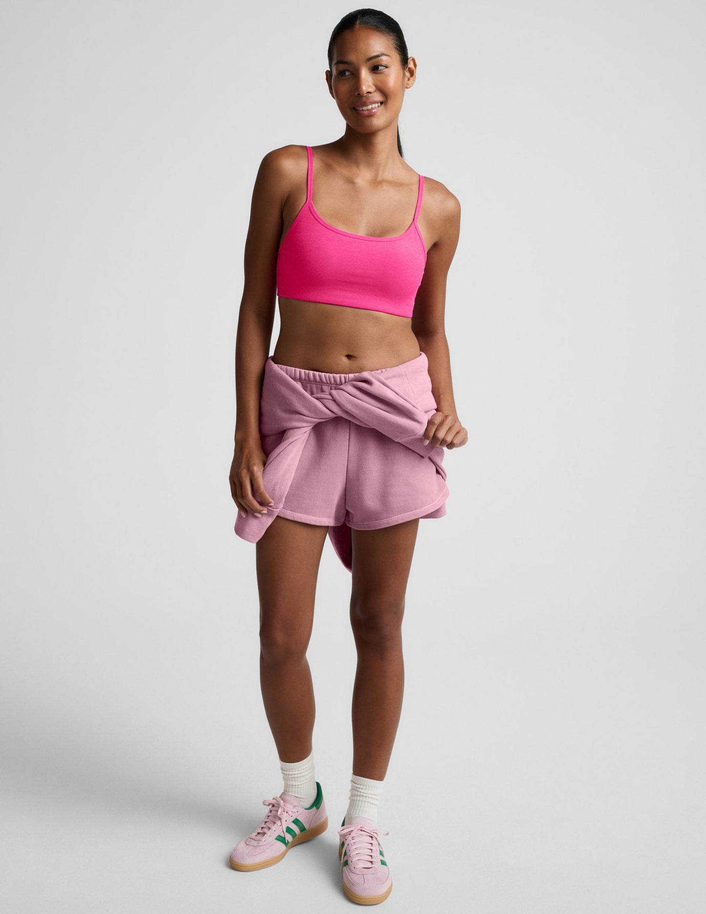Woman wearing a pink sports bra and shorts on a plain background.