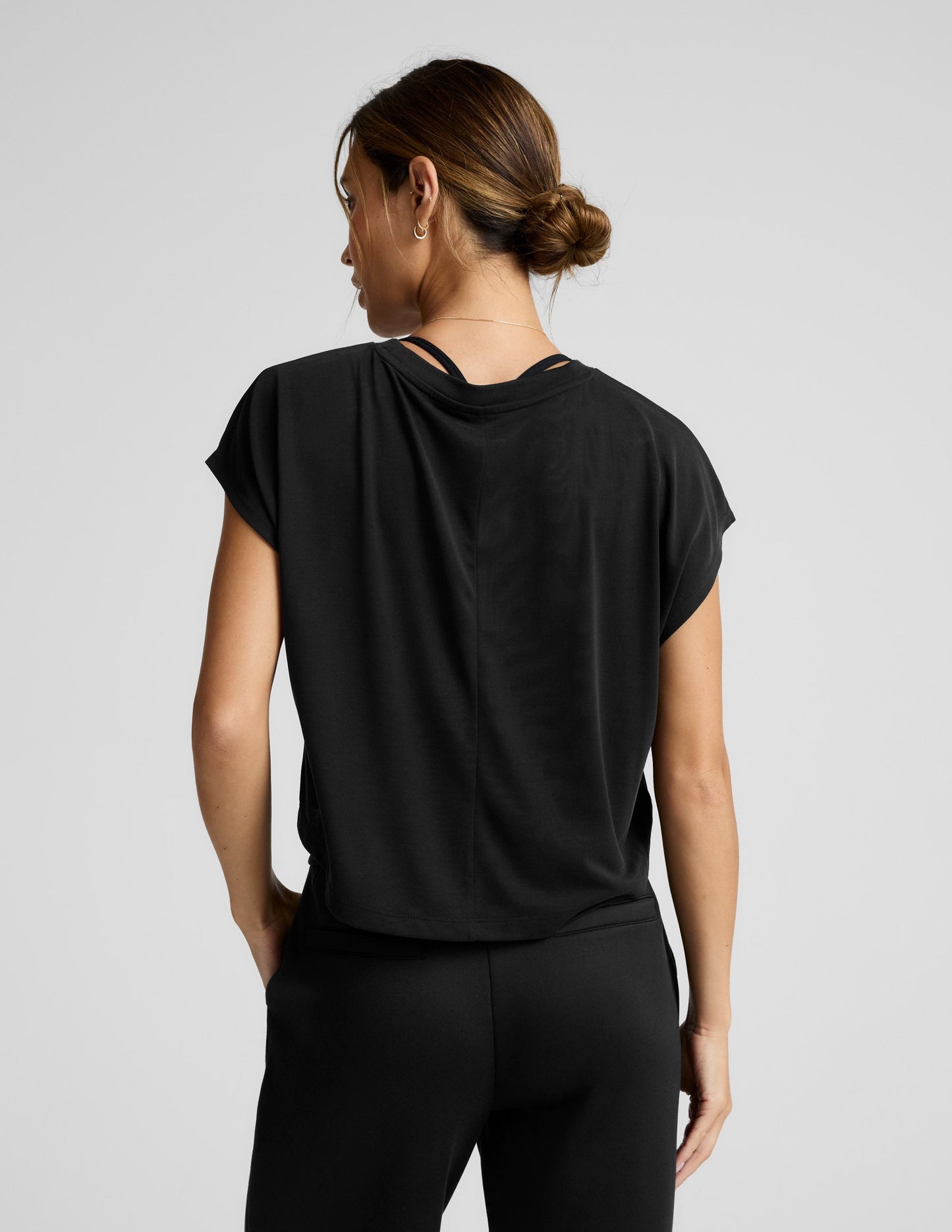 Person wearing a black cropped tee and pants on a light gray background.