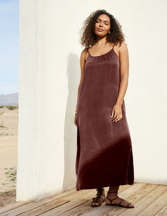 Woman wearing a brown cupro maxi dress leaning against a wall.