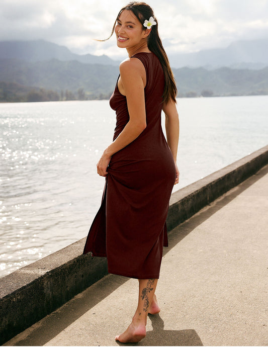 Woman in a brown dress standing by a lake with mountains in the background.
