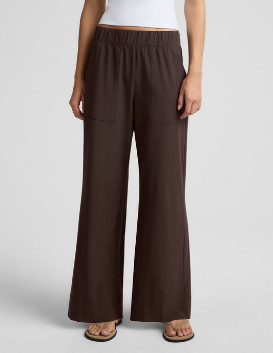 Woman wearing a white halter tank top and brown wide leg pants against a plain studio background.