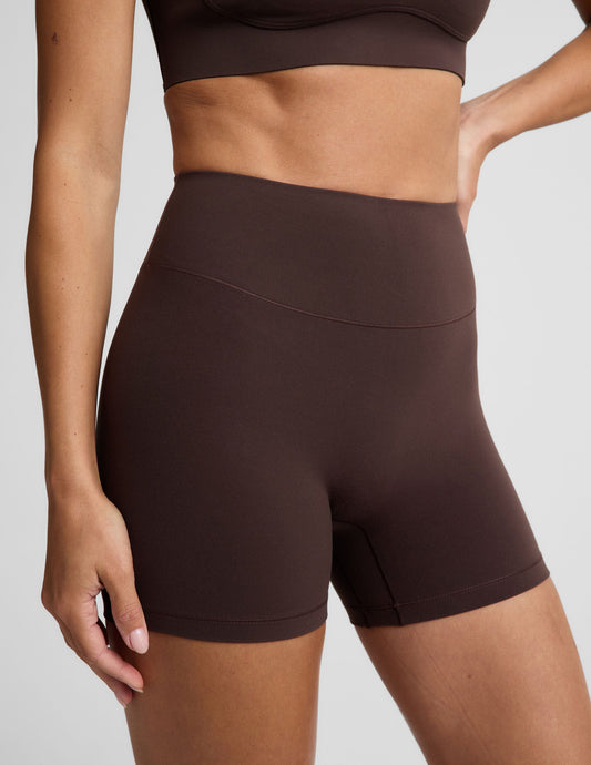 Woman wearing a brown sports bra and brown biker shorts against a plain background.