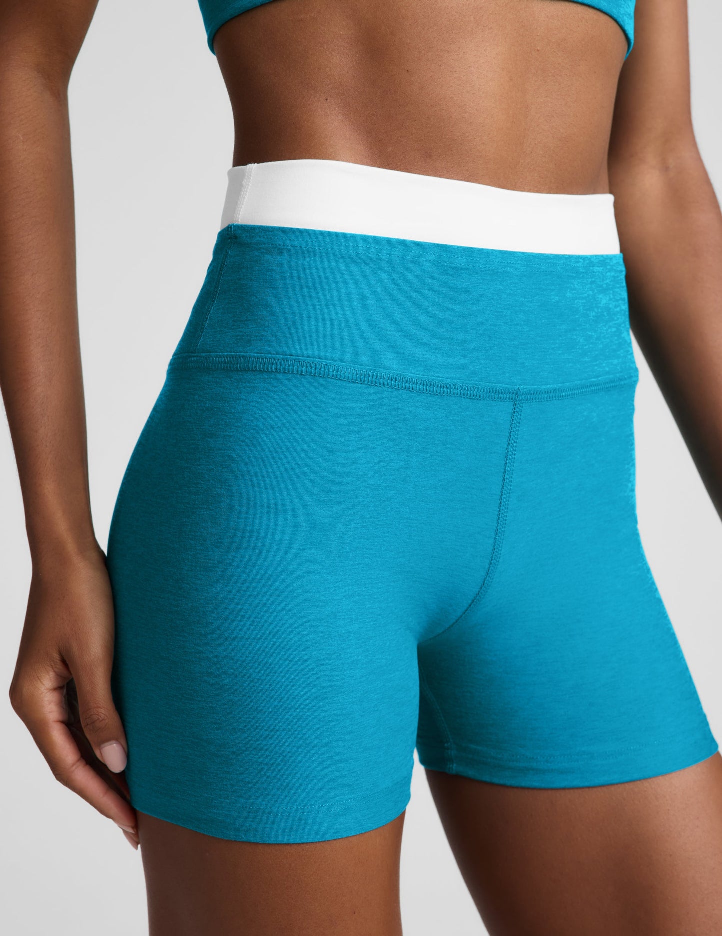 Woman wearing a. blue cropped tank and biker shorts with a white lining against a plain background.