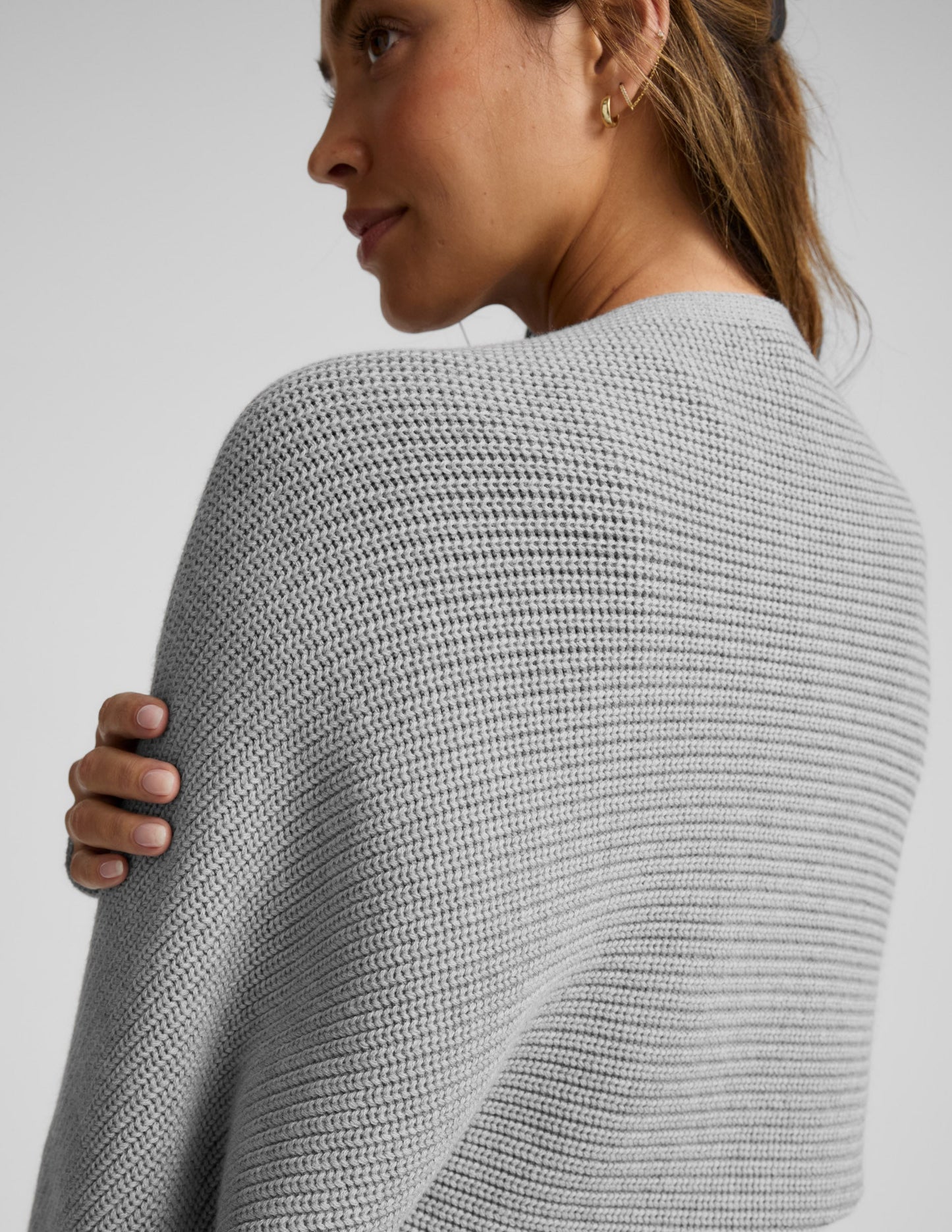 Woman wearing a gray shrug on a light gray background.