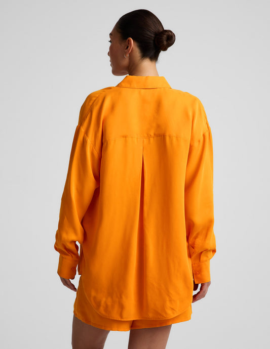 Woman wearing an orange button down shirt and orange shorts against a plain background.