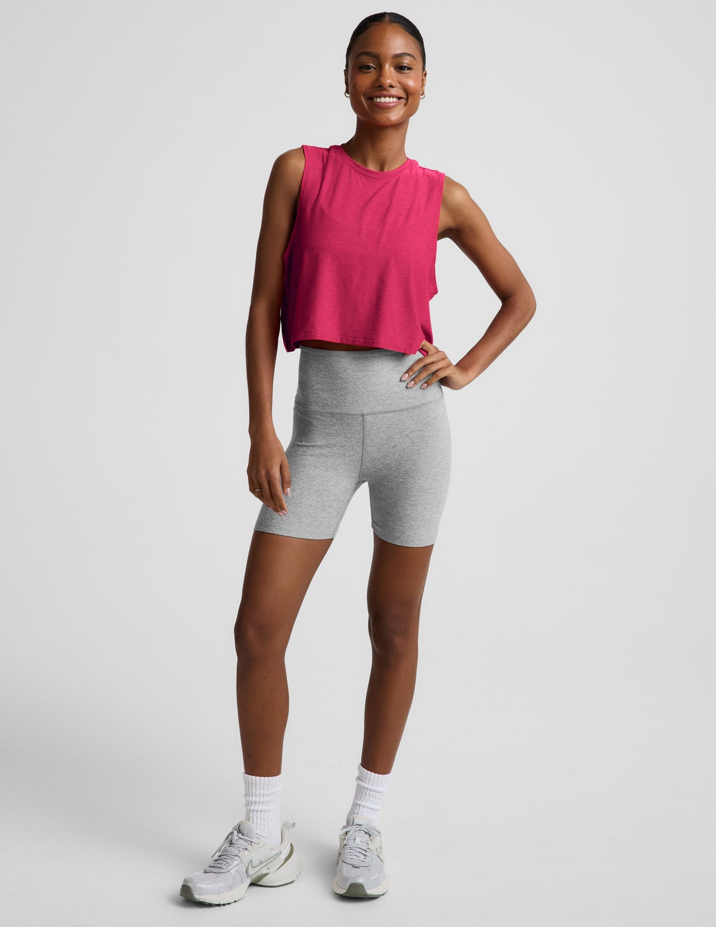 Woman wearing a red cropped tank and gray biker shorts against a plain background.