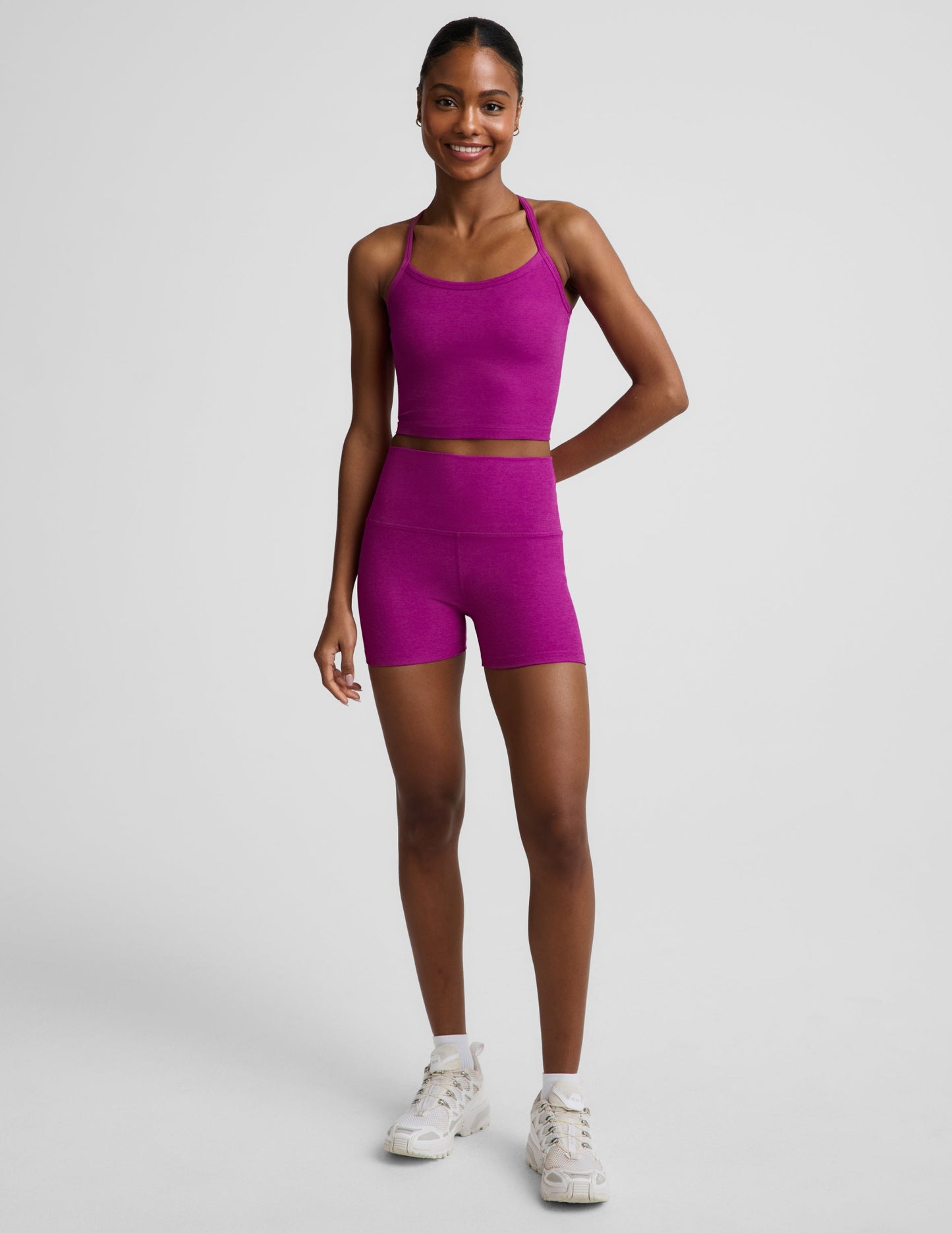 Woman wearing a purple racerback cropped tank and biker shorts against a plain background.