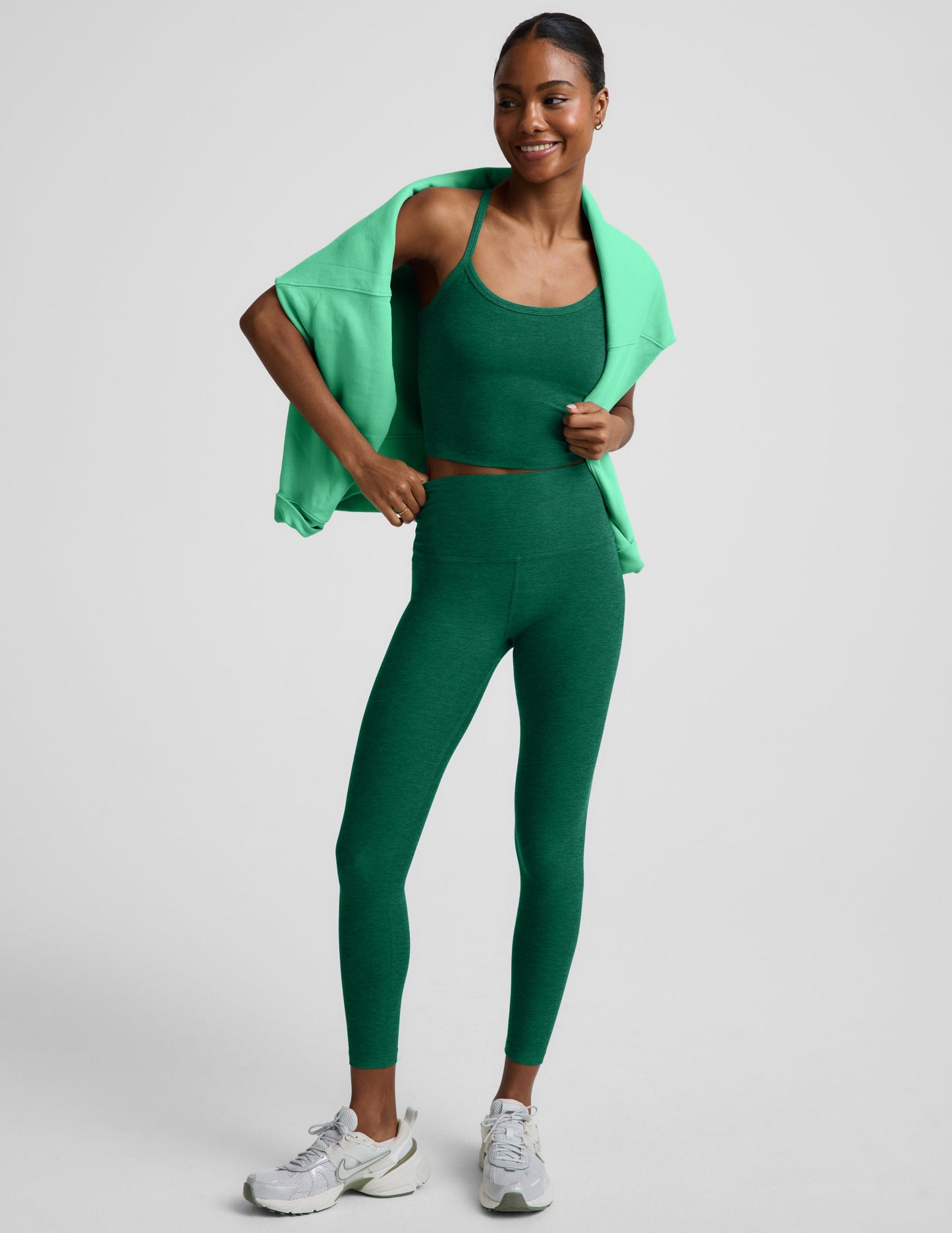 Woman wearing a green cropped racerback tank and leggings against a plain background.