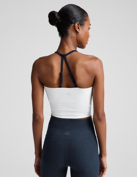 Woman wearing a white v-neck strappy cropped tank and blue biker shorts against a plain background.
