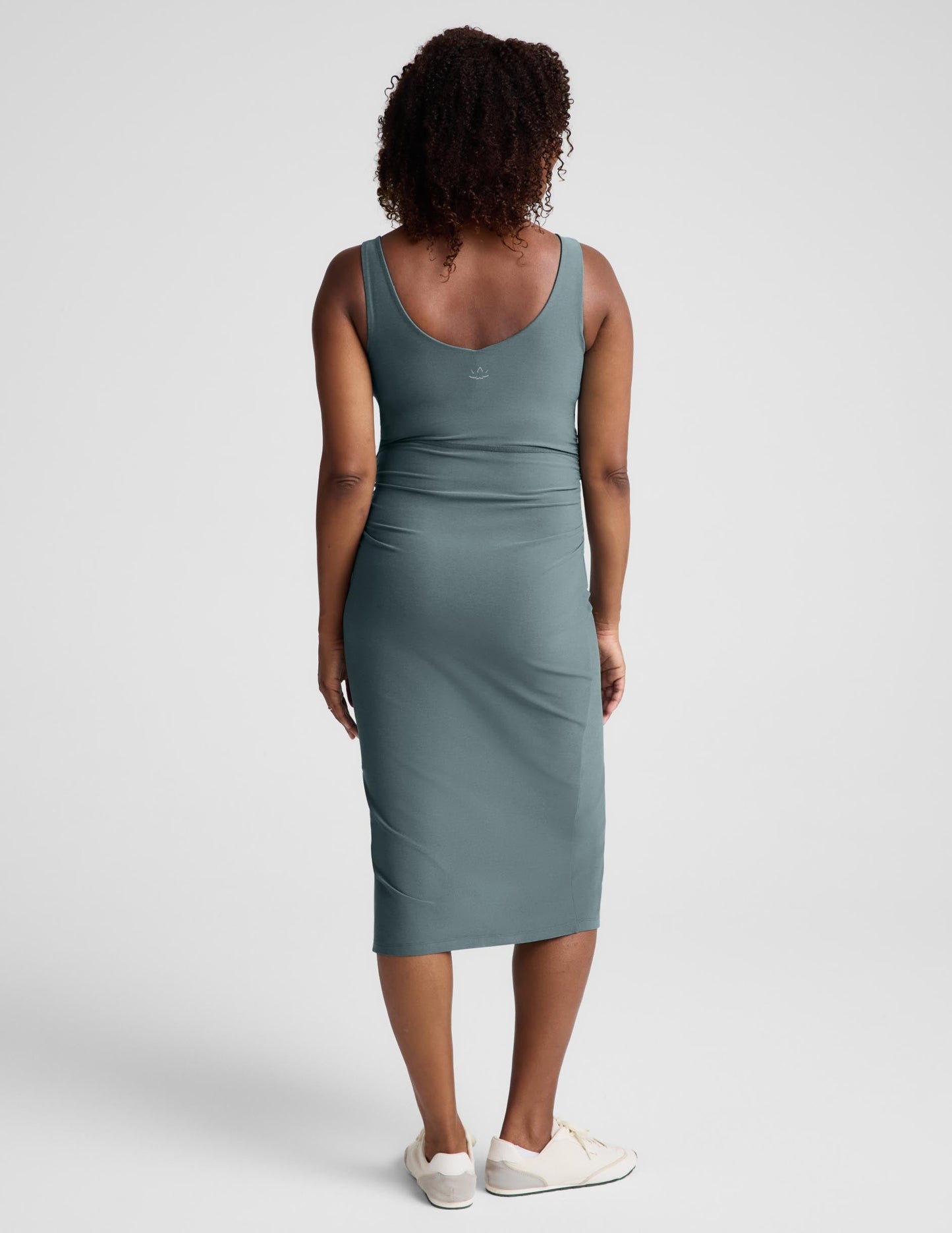 Pregnant woman wearing a green maternity midi length tank dress with a front side slit against a plain background.