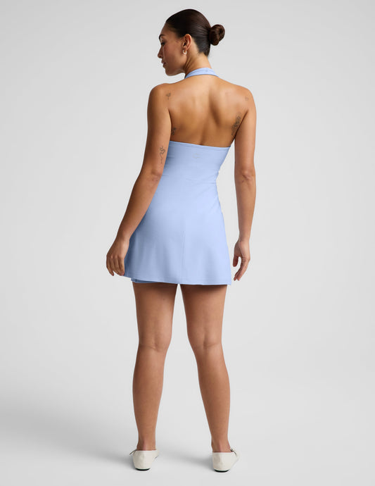 Woman wearing a light blue halter mini dress against a plain background.