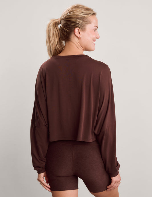 Woman wearing a brown long sleeve top and brown biker shorts against a plain background.