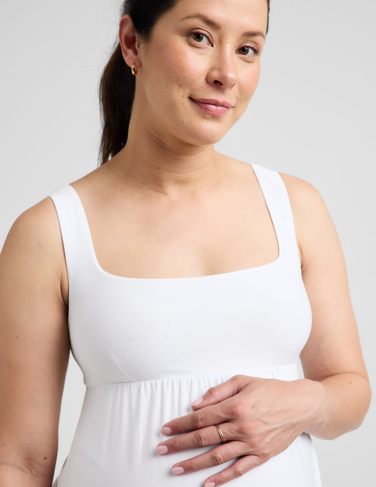 Pregnant woman wearing a white maxi dress against a plain background.