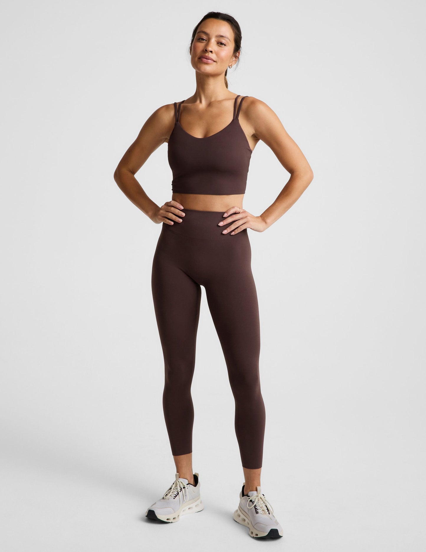Woman wearing a brown cropped tank and midi leggings on an plain studio background.
