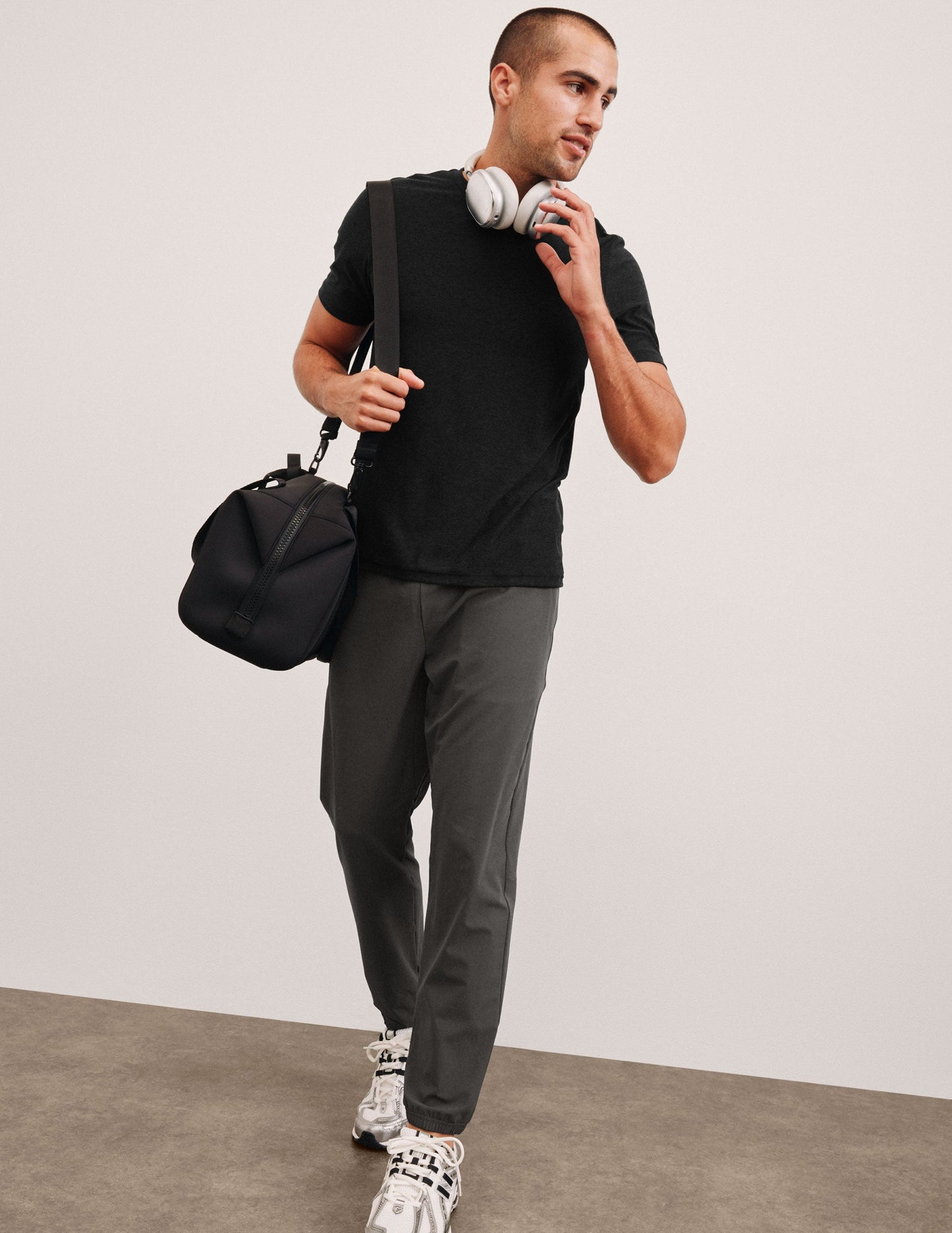 Man wears gray On The Go Men's Jogger with elastic cuffs, walking with a gym bag and headphones. Relaxed, casual style.