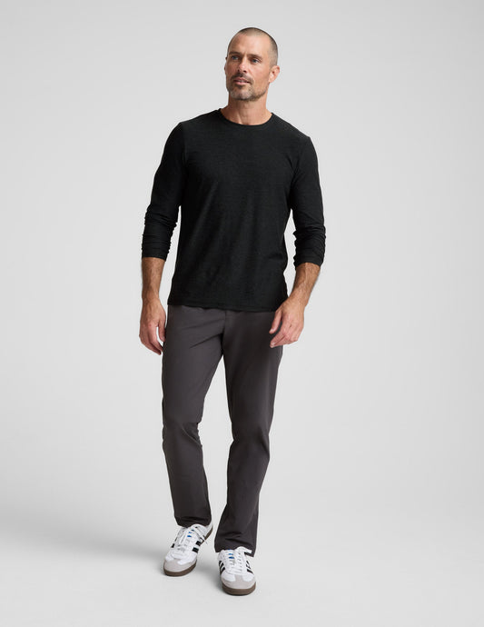 Man walking in dark charcoal Men's All Terrain Pant with a straight-leg fit, black long-sleeve shirt, and white sneakers.