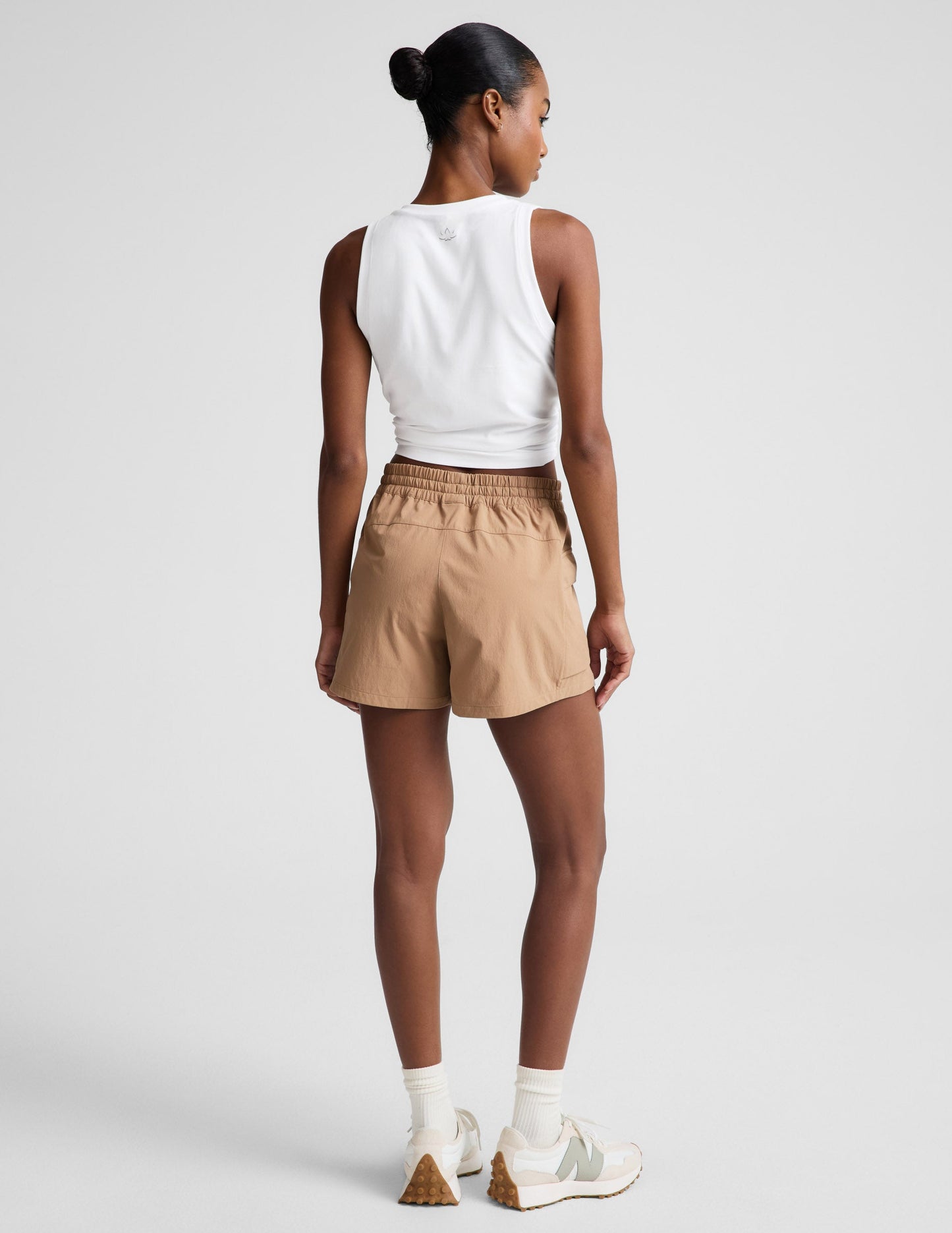 Woman wearing tan Peak 3" Short with a white cropped tank top, rear view showing the gathered elastic waistband.