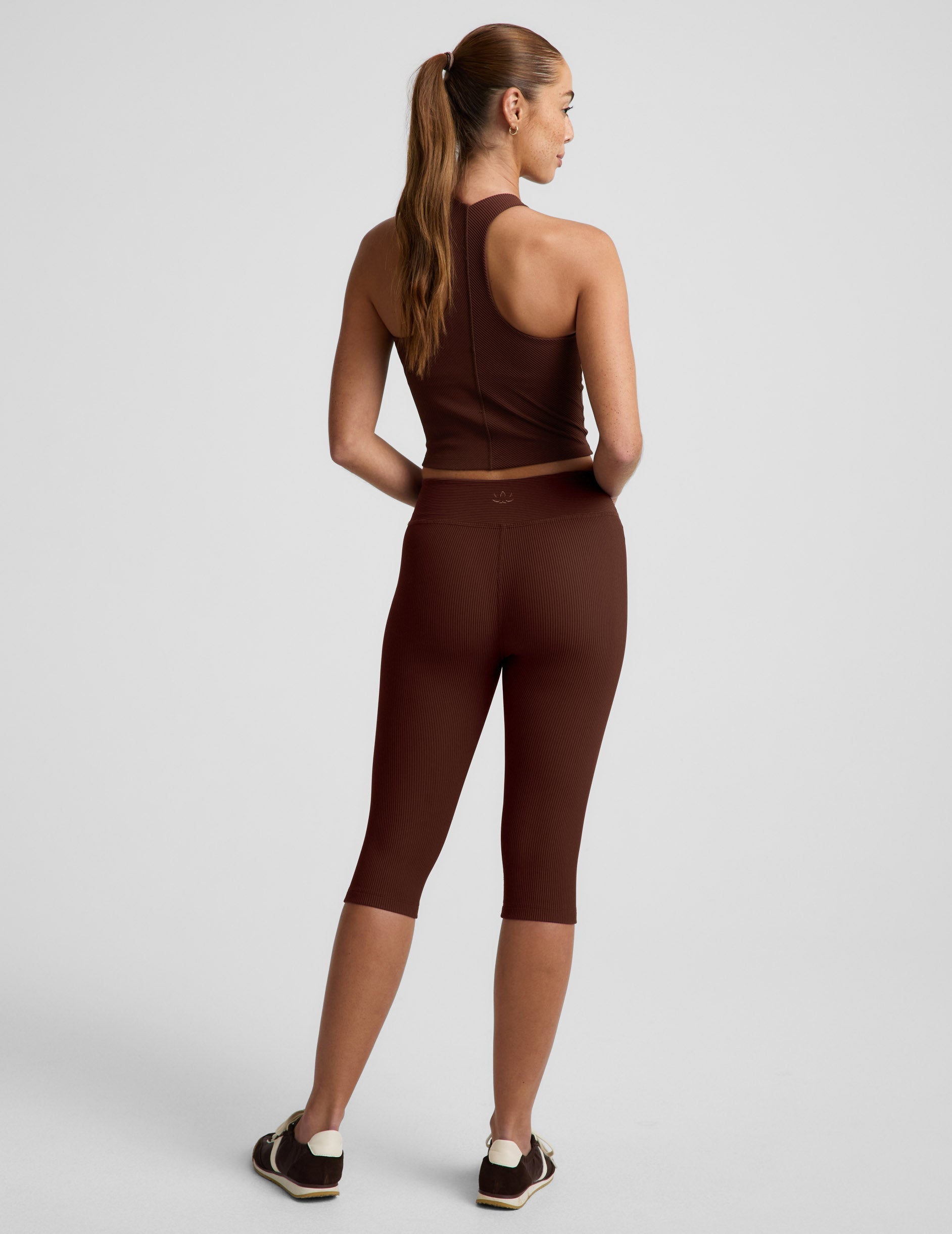Woman wearing brown Impulse™ Ribbed V-Waist Pedal Pusher Legging with a matching tank top, rear view.