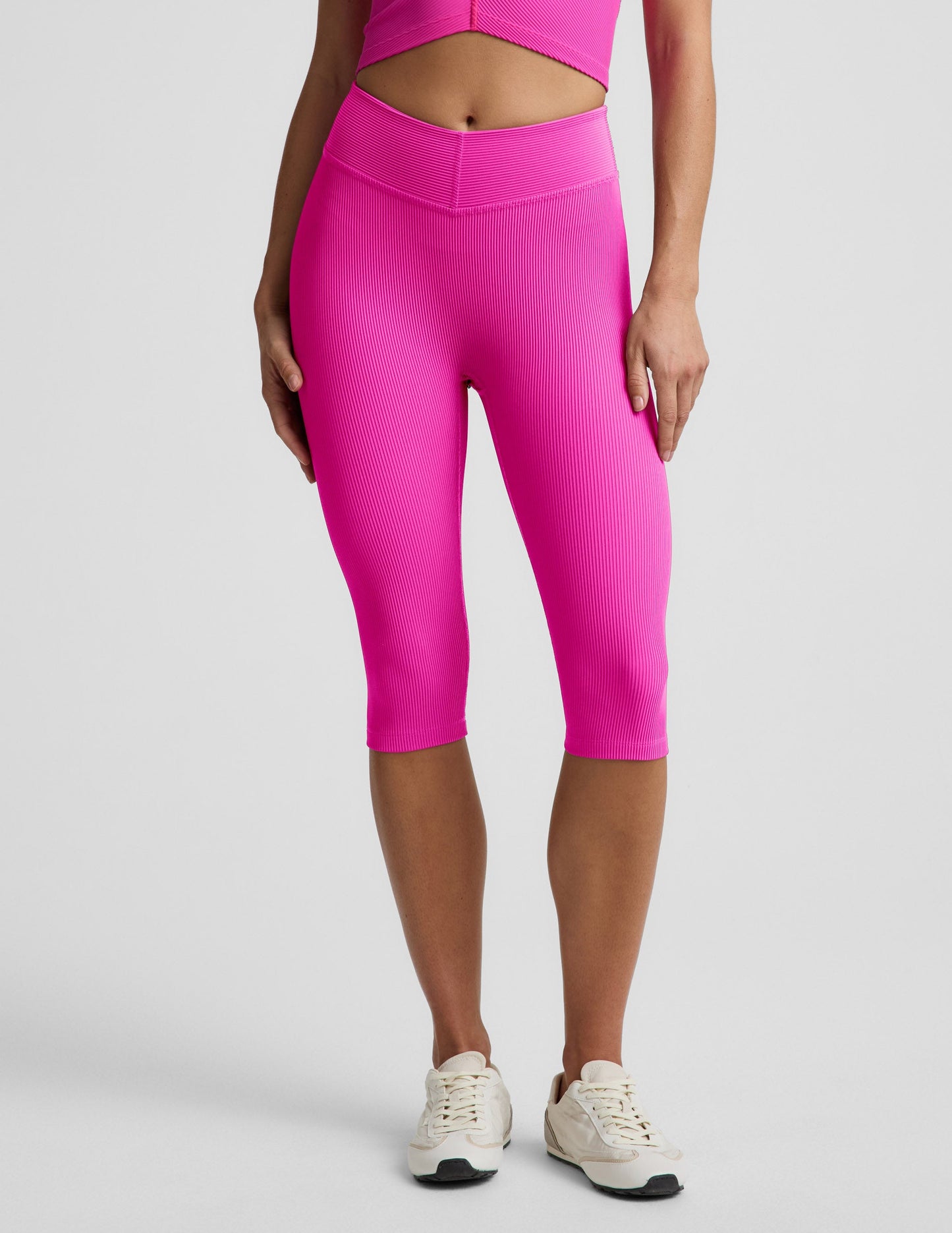 Woman wearing Pink Impulse Ribbed V-Waist Pedal Pusher Legging paired with a matching top and cream sneakers.