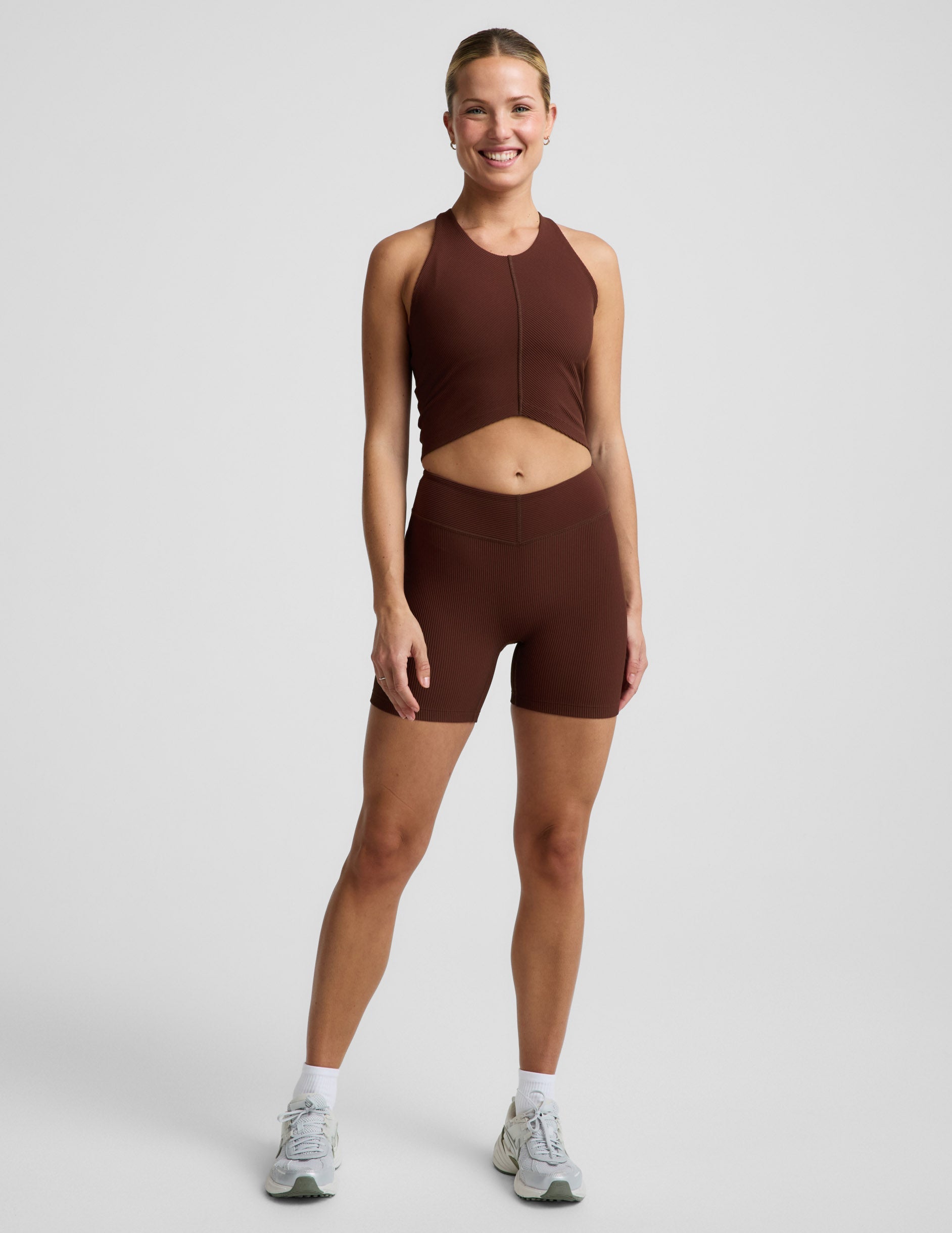 Woman wearing a brown ribbed cropped tank and brown ribbed shorts against a plain background.