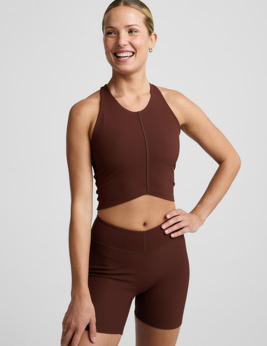 Woman wearing a brown ribbed cropped tank and brown ribbed shorts against a plain background.