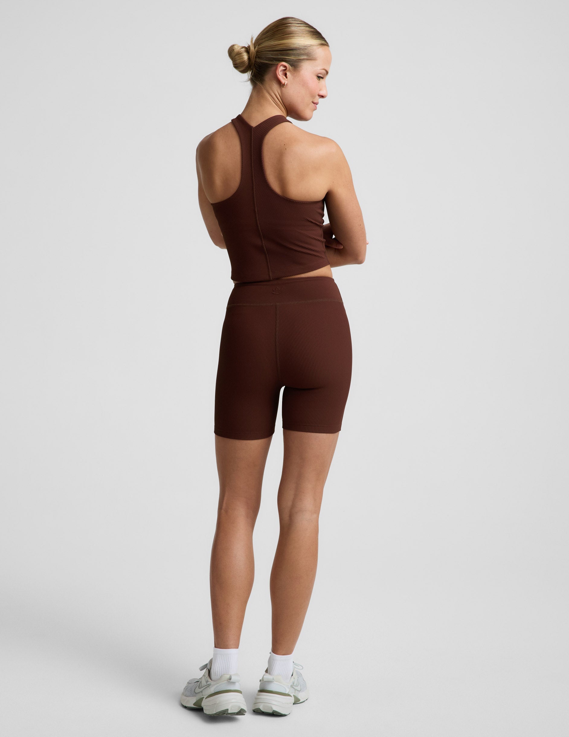 Woman wearing a brown ribbed cropped tank and brown ribbed shorts against a plain background.