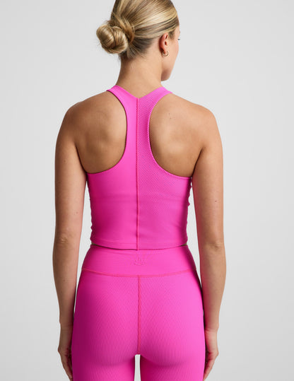 Woman wearing a bright pink ribbed cropped tank top and ribbed biker shorts against a plain background.
