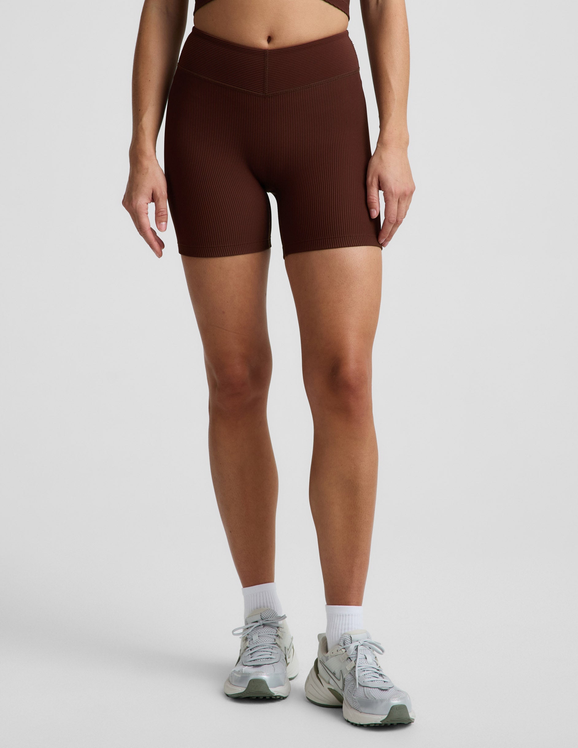 Woman wearing Brown Impulse Ribbed V-Waist 5" Biker Short™ paired with white socks and grey sneakers.