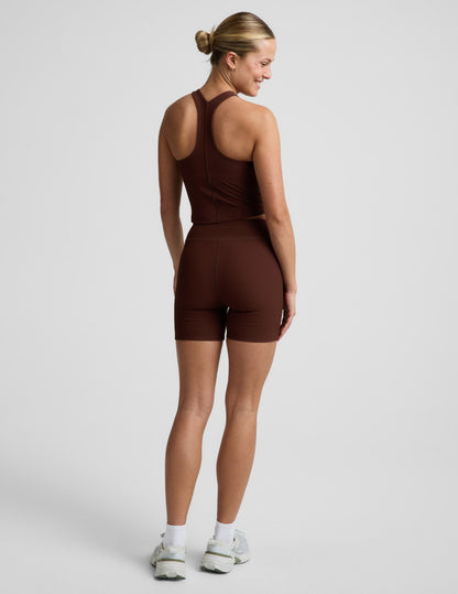 Woman wearing Brown Impulse™ Ribbed V-Waist 5" Biker Short paired with a matching tank top and sneakers, rear view.