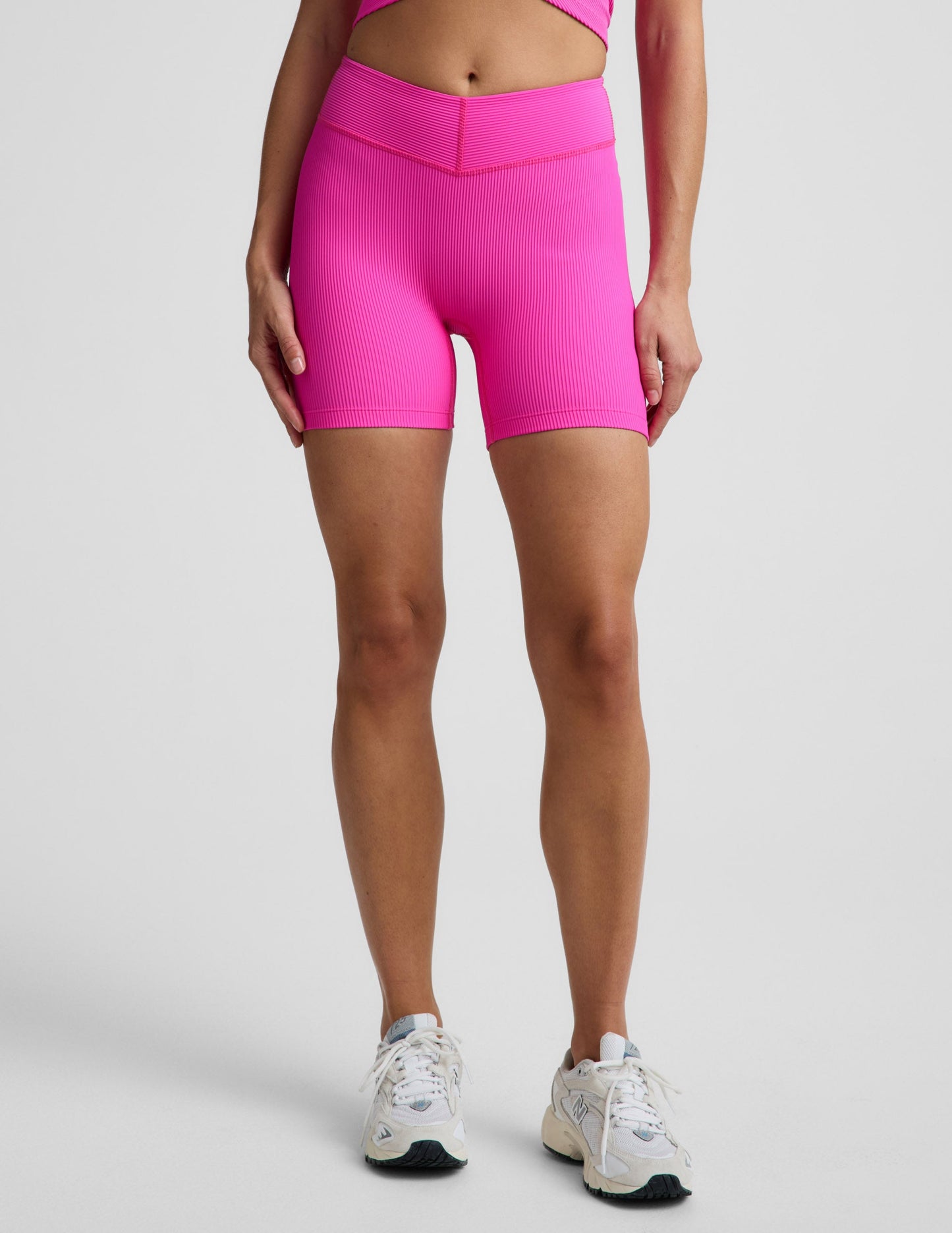 Woman wearing Pink Impulse Ribbed V-Waist 5" Biker Short paired with a matching pink crop top and cream sneakers.