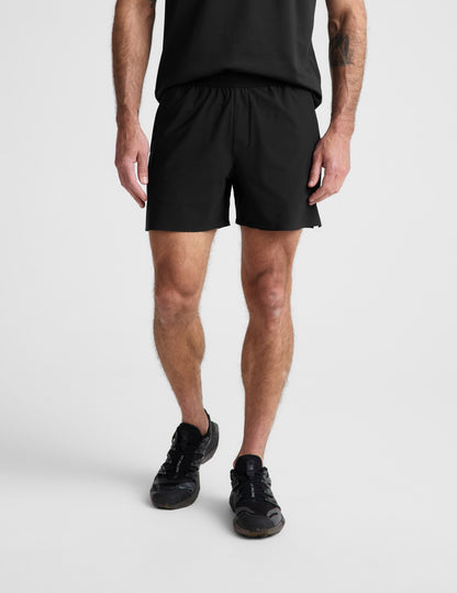 Man wearing black WarpLite™ Range Lined Short with an elastic waistband, paired with a black t-shirt and sneakers.