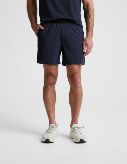 Man wearing Navy WarpLite Range Lined Short™ with an elastic waistband, paired with a matching top and cream sneakers.