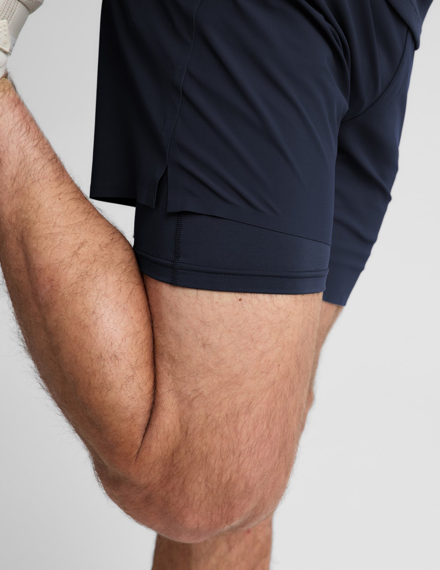 Man wearing Navy WarpLite Range Lined Short™ with cream sneakers, side profile showing the layered liner while stretching.