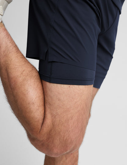 Man wearing Navy WarpLite Range Lined Short™ with cream sneakers, side profile showing the layered liner while stretching.