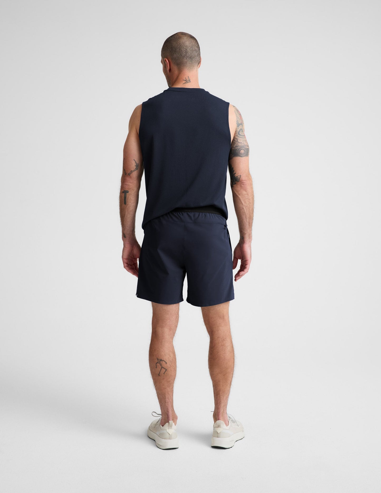 Man wearing Navy WarpLite Range Lined Short™ from a Rear view, paired with a navy tank top and cream sneakers.