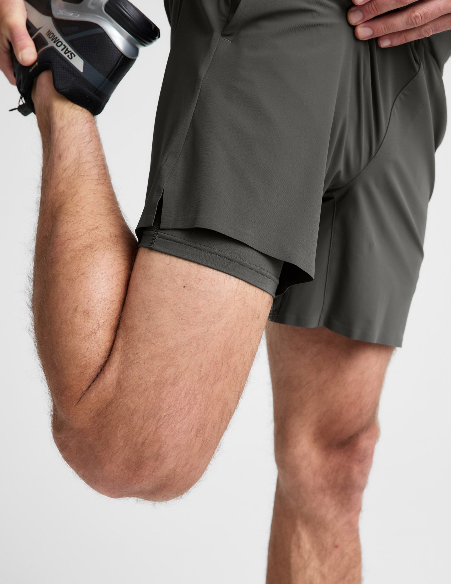 Man wearing Olive WarpLite™ Range Lined Short with visible inner liner while stretching, paired with a black sneaker.