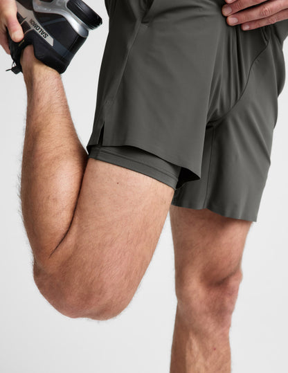 Man wearing Olive WarpLite™ Range Lined Short with visible inner liner while stretching, paired with a black sneaker.