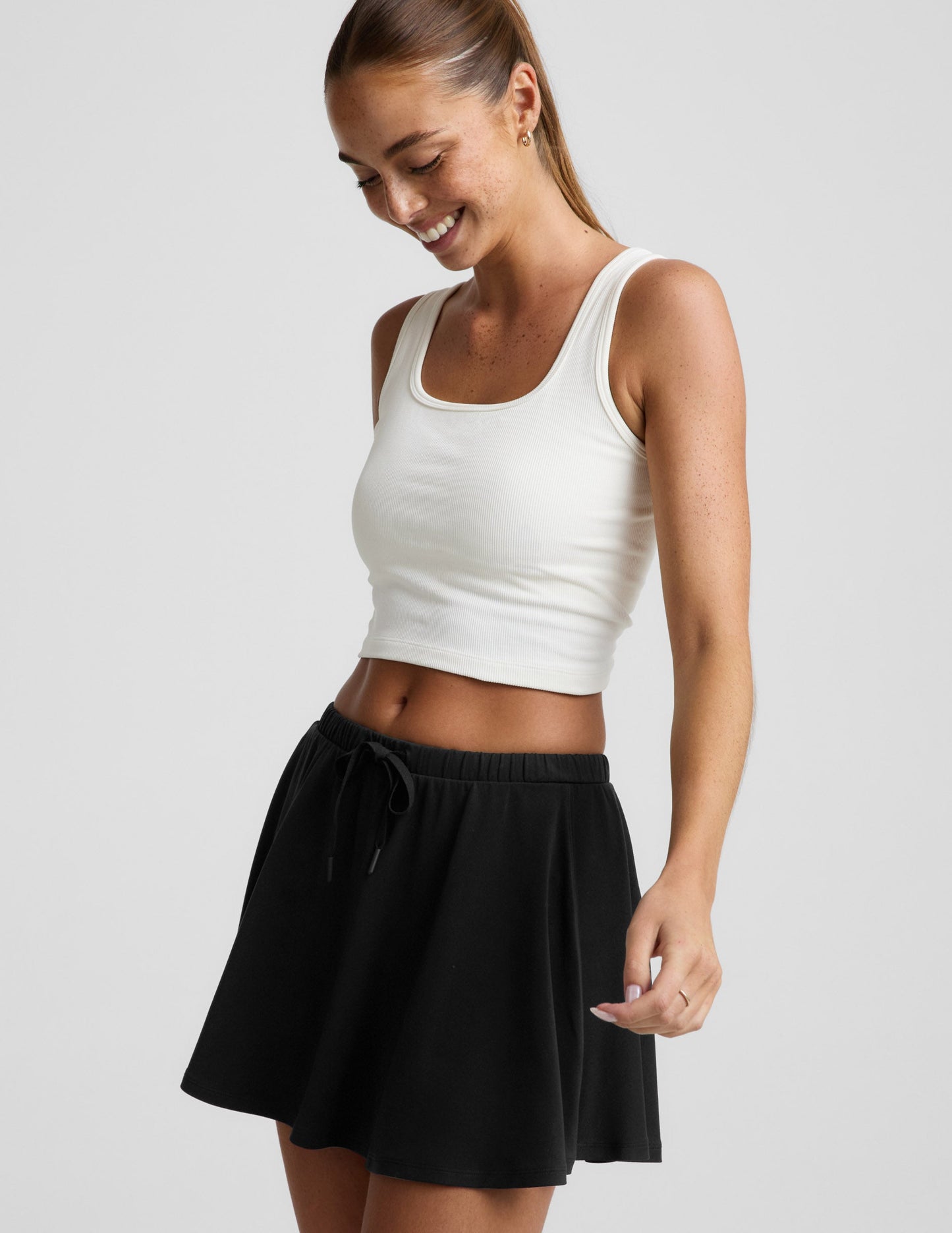 Woman wearing the Black Sport Active Drawcord Mini Skirt paired with a white tank top, featuring a drawstring waist.