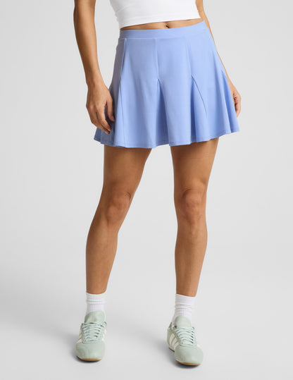 Woman wearing Blue Flounce This Way Skirt™ with a white top and green sneakers, featuring a high-waisted flared mini hem.