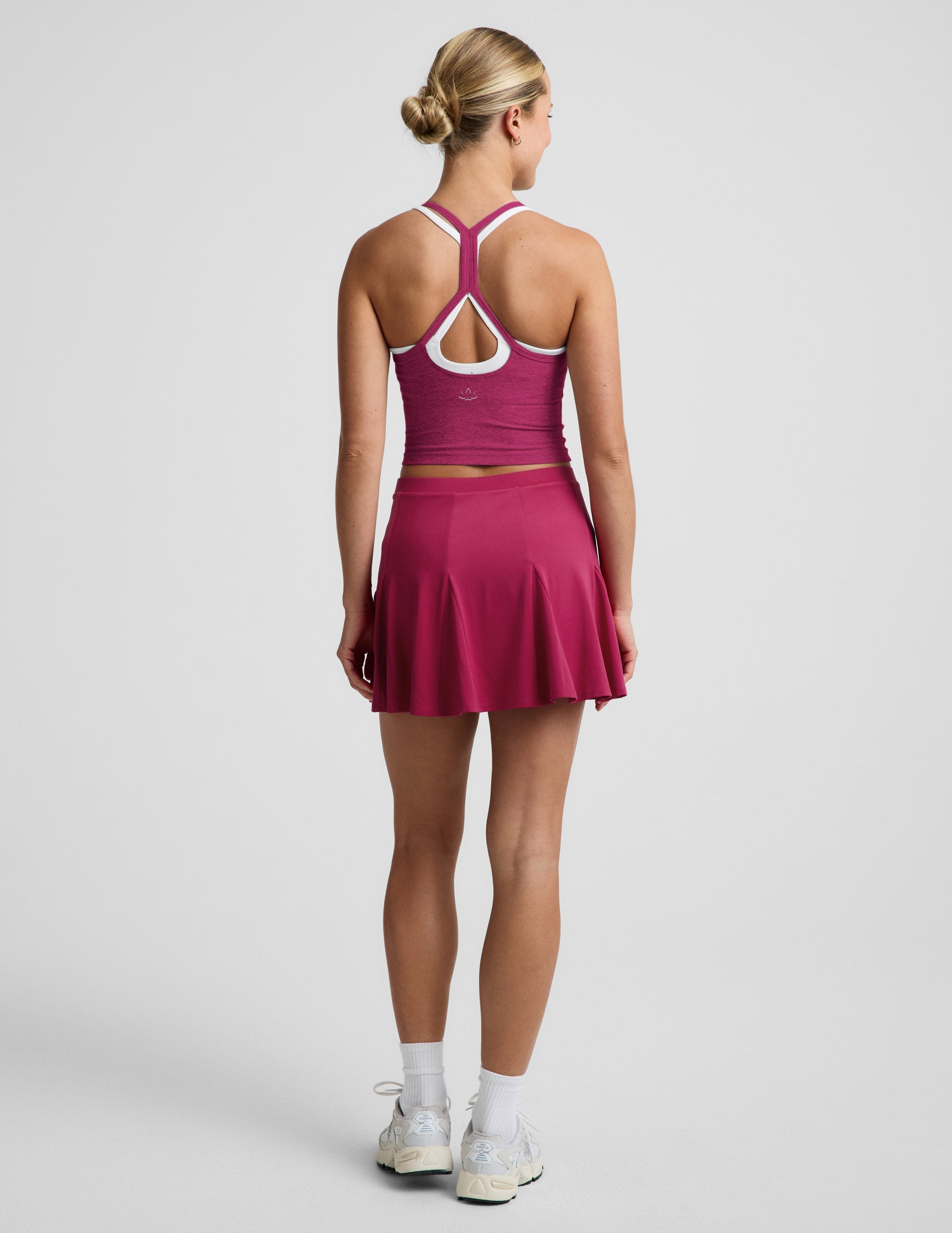 Woman wearing Fuchsia Flounce This Way Skirt™, rear view, paired with a purple racerback top and white sneakers.
